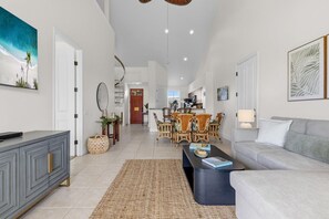 A spacious living room with a grey sofa, a coffee table, and a dining area with wooden chairs. - Top Floor Fairway Villas Condo | 2BR + Loft | Sleeps 8 | Golf Course Views (Waikoloa)