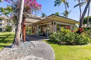 A covered outdoor area with a concrete path leading to a building with glass doors. - Top Floor Fairway Villas Condo | 2BR + Loft | Sleeps 8 | Golf Course Views (Waikoloa)