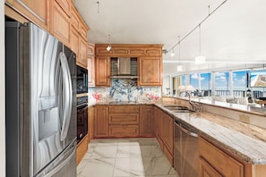 Eine moderne Küche mit Holzausbau, einem Edelstahlkühlschrank, einer gefliesten Spritzschutzwand und einem großen Fenster mit Blick auf eine Stadtlandschaft.