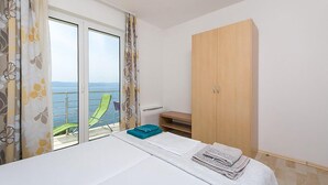 Une chambre à coucher avec un lit, une armoire, un balcon avec une chaise et une vue sur la mer.