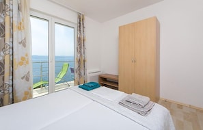 A bedroom with a bed, a wardrobe, a balcony with a chair, and a view of the sea. - Cozy apartment in Brela with WiFi (Brela)