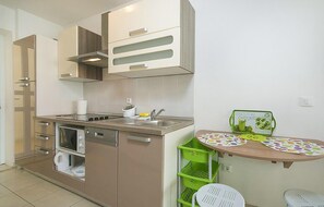 A modern kitchen with a dishwasher, stove, and a small dining area with a table and chairs. - Cozy apartment in Brela with WiFi (Brela)
