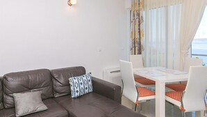 Un salon avec un canapé en cuir marron, deux coussins à motifs, une table blanche et des chaises à rayures orange et blanches, ainsi qu’une fenêtre avec des rideaux.