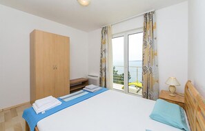 Ein Schlafzimmer mit Bett, einem Holzschrank, einem Fenster mit Vorhängen und Blick auf das Meer.