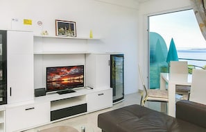 Ein modernes Wohnzimmer mit Flachbildfernseher, weißen Schränken und einer Glastür, die auf einen Balkon mit Meerblick führt.