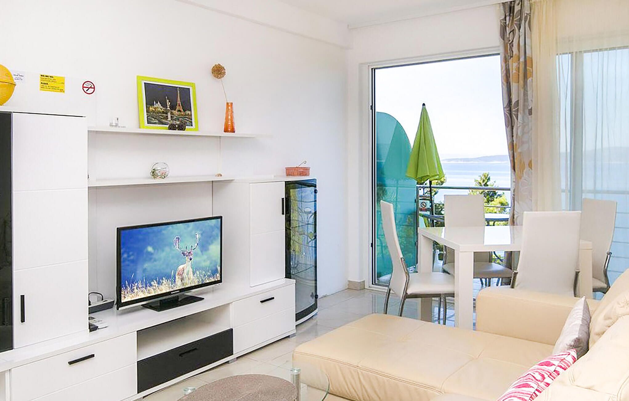 Un salon moderne doté d’un téléviseur à écran plat, d’un canapé, d’un coin repas avec une table et des chaises, et d’un balcon offrant une vue agréable.