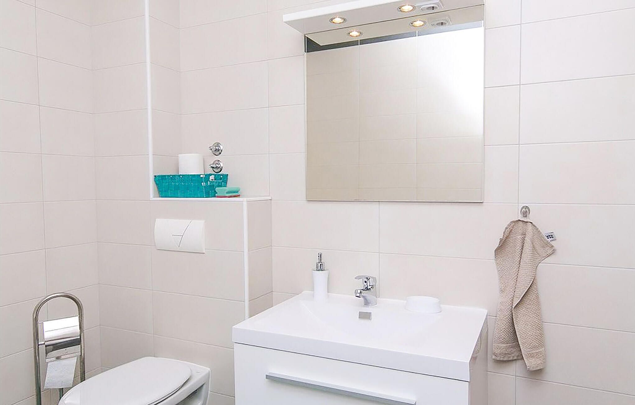 Ein Badezimmer mit Waschbecken, Spiegel und Toilette. Ein Handtuch hängt an der Wand und ein Ablagefach enthält Toilettenartikel.