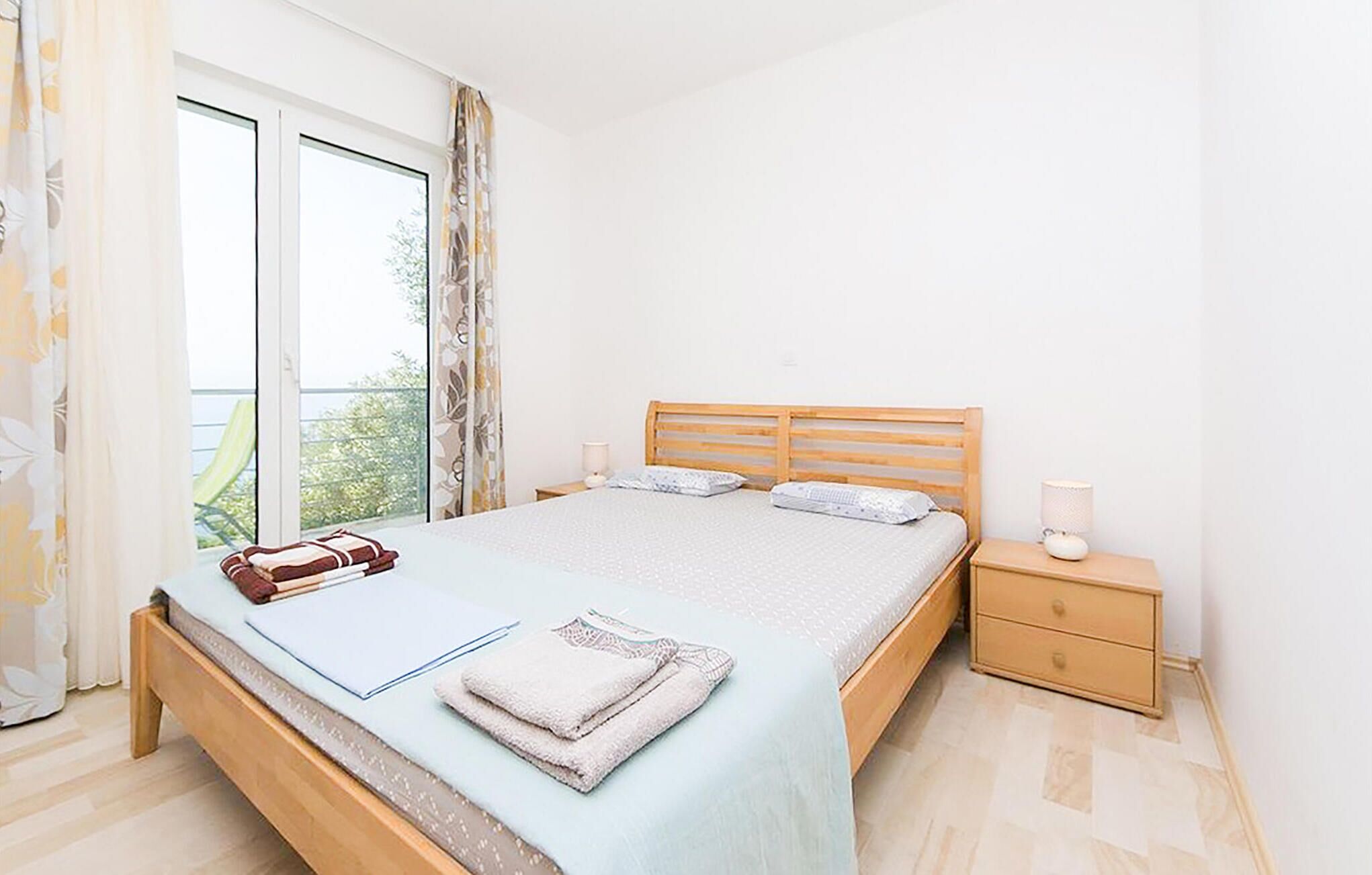 Un dormitorio con cama, mesita de noche, ventana con cortinas y vistas al exterior.