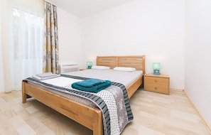 A bedroom with a wooden bed, a nightstand with a lamp, and a window with curtains. - 2 bedroom gorgeous apartment in Brela (Brela)