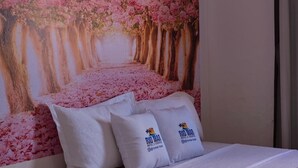 Ένα δωμάτιο ξενοδοχείου με ένα κρεβάτι, δύο μαξιλάρια με το λογότυπο του ξενοδοχείου και μια τοιχογραφία με άνθη κερασιάς.