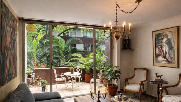 Een ruime woonkamer met een groot raam, een kroonluchter en een eethoek met buitenplanten.