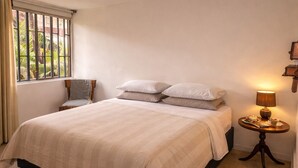 Een opgemaakt bed met een beige sprei, een nachtkastje met een lamp en een stoel.