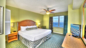 Ein Hotelzimmer mit Bett, Schreibtisch, Fernseher und einem Fenster mit Blick aufs Meer.