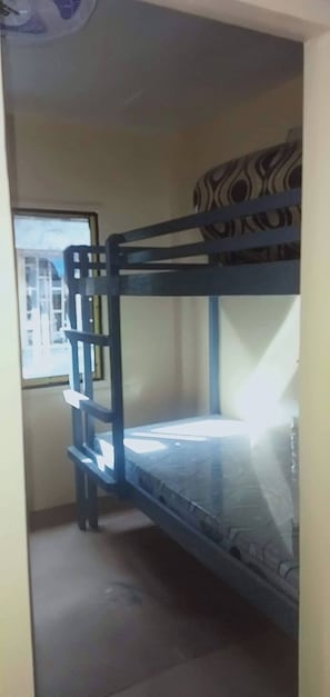 A bunk bed with a patterned pillow, a window with a view, and a fan on the ceiling.