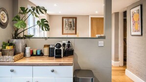 Une cuisine compacte avec un plan de travail en bois, une machine à café, une plante en pot et une poubelle.