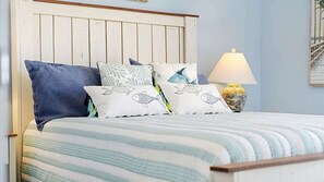 A bed with striped bedding and multiple pillows, a wooden headboard, a bedside lamp, and a framed picture on the wall. - Horizon South Resort -  Relaxation Awaits! (Panama City Beach)