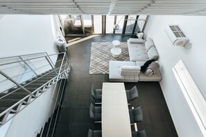 A modern interior with a sofa, coffee table, and dining area, featuring a staircase and large windows.