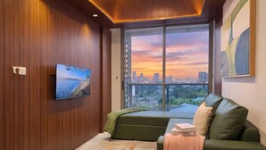 Une chambre moderne dotée d’une grande fenêtre, d’un canapé vert, d’un téléviseur à écran plat et offrant une vue sur le paysage urbain.
