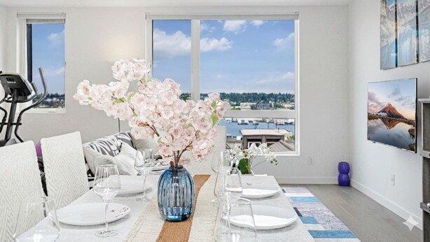 A modern dining room with a view of a marina, a dining table set with white plates and glasses, and a vase with flowers.