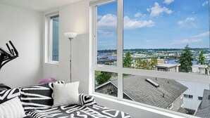A modern room with a large window offering a city view, a ceiling fan, and a bed with patterned bedding.