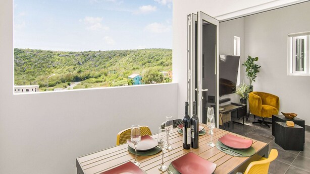 Een eethoek met een tafel voor vier personen, uitzicht op een groen landschap en een gele stoel.