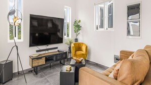 Een moderne woonkamer met een grote flatscreen televisie, een gele fauteuil, een bruine bank en een klein bijzettafeltje.