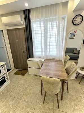A compact living space with a dining table, chairs, a sofa, a clock, and a microwave.