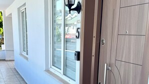 A modern building entrance with a wooden door, a black wall-mounted light fixture, and a window with a view of a neighboring property. - ESG • 5-Min Walk to Göynük Beach • Mountain View Terrace Studio (Goynuk)