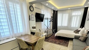 Quarto de hotel moderno com uma cama, um sofá, uma mesa de jantar com cadeiras, uma televisão e uma escrivaninha.