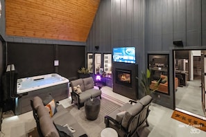 Ein moderner Lounge-Bereich mit Kamin, bequemen Sitzgelegenheiten und einem Fernseher, der den Titel 'The Watchful Eye' zeigt.