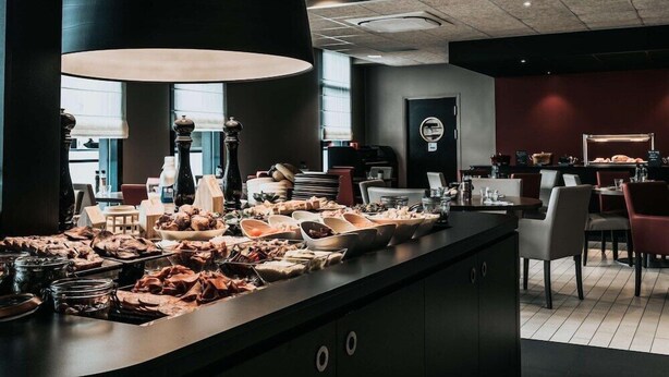 A buffet setup with various food items, a large pendant light, and a modern interior design. - Campanile Rouen Mermoz (Rouen)