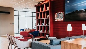A modern lounge area with seating, a bookshelf, and a flat-screen TV. - Campanile Rouen Mermoz (Rouen)