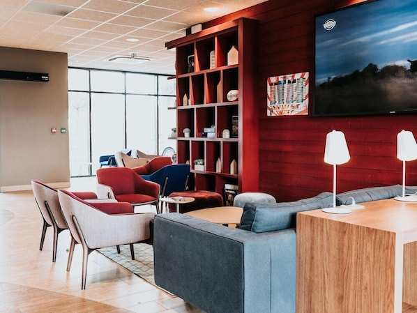 A modern lounge area with seating, a bookshelf, and a flat-screen TV. - Campanile Rouen Mermoz (Rouen)