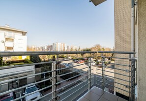 Vista desde un balcón sobre un estacionamiento con varios coches, un edificio de fachada de ladrillo y un cielo despejado.