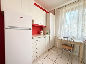 Eine kleine Küche mit einem Kühlschrank, einem Wasserkocher und einem Tisch mit einem Stuhl.