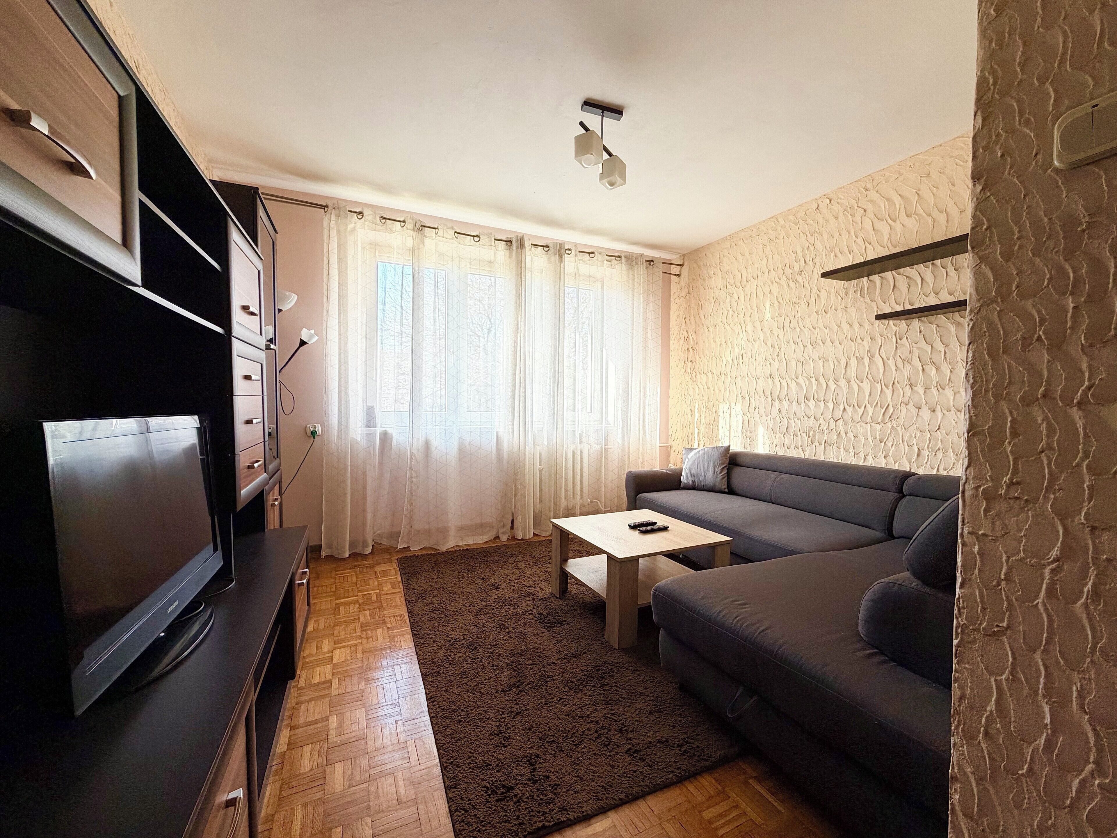A modern living room with a flat-screen TV, a sofa, a coffee table, and a patterned rug.