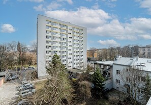 Un edificio residencial de varios pisos con una cuadrícula de ventanas y balcones, rodeado de árboles y otros edificios.