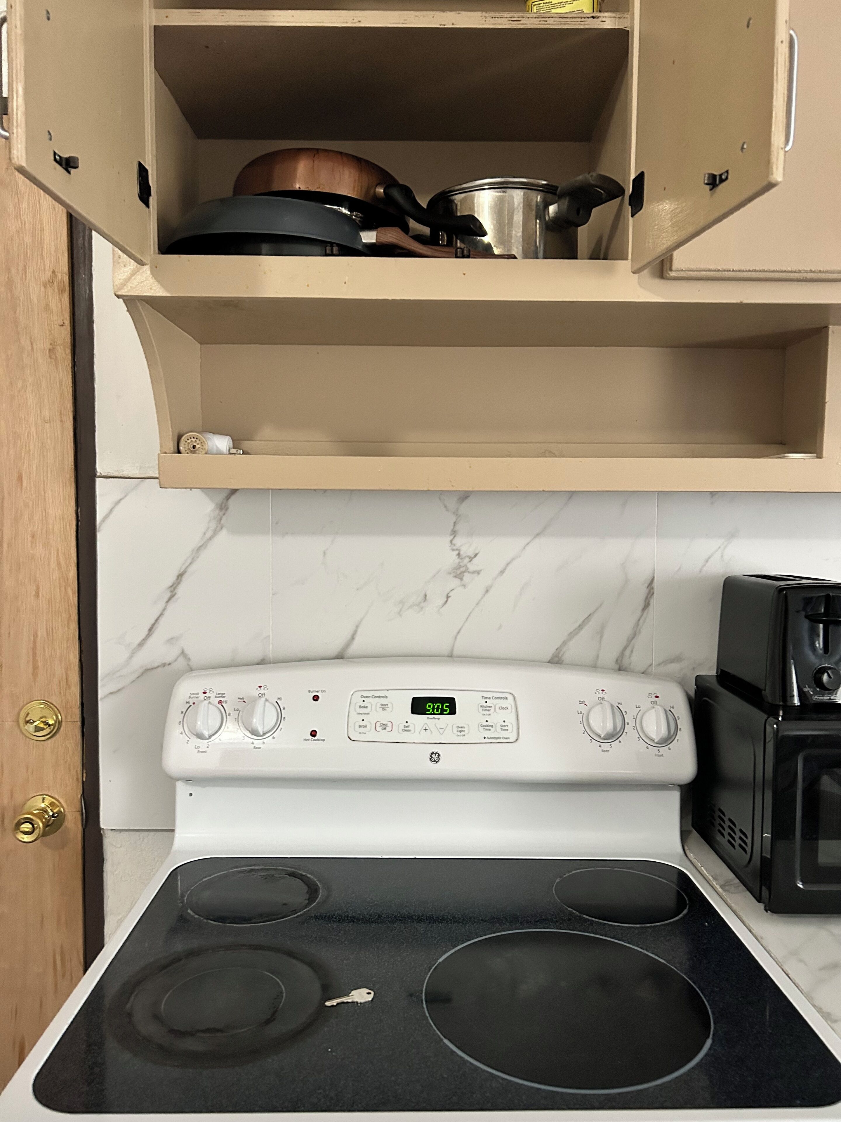 A kitchen with a white stove, a microwave, and a cabinet above the stove containing pots and pans.