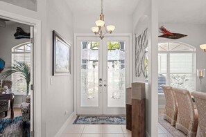 A spacious entryway with a chandelier, a glass door, and a view to the outside. - A Shore Thing - Direct Gulf Access Southern Facing Villa (Cape Coral)