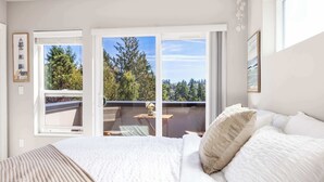 Una camera da letto con un letto grande, un balcone che offre vista su alberi e una finestra con una cornice.