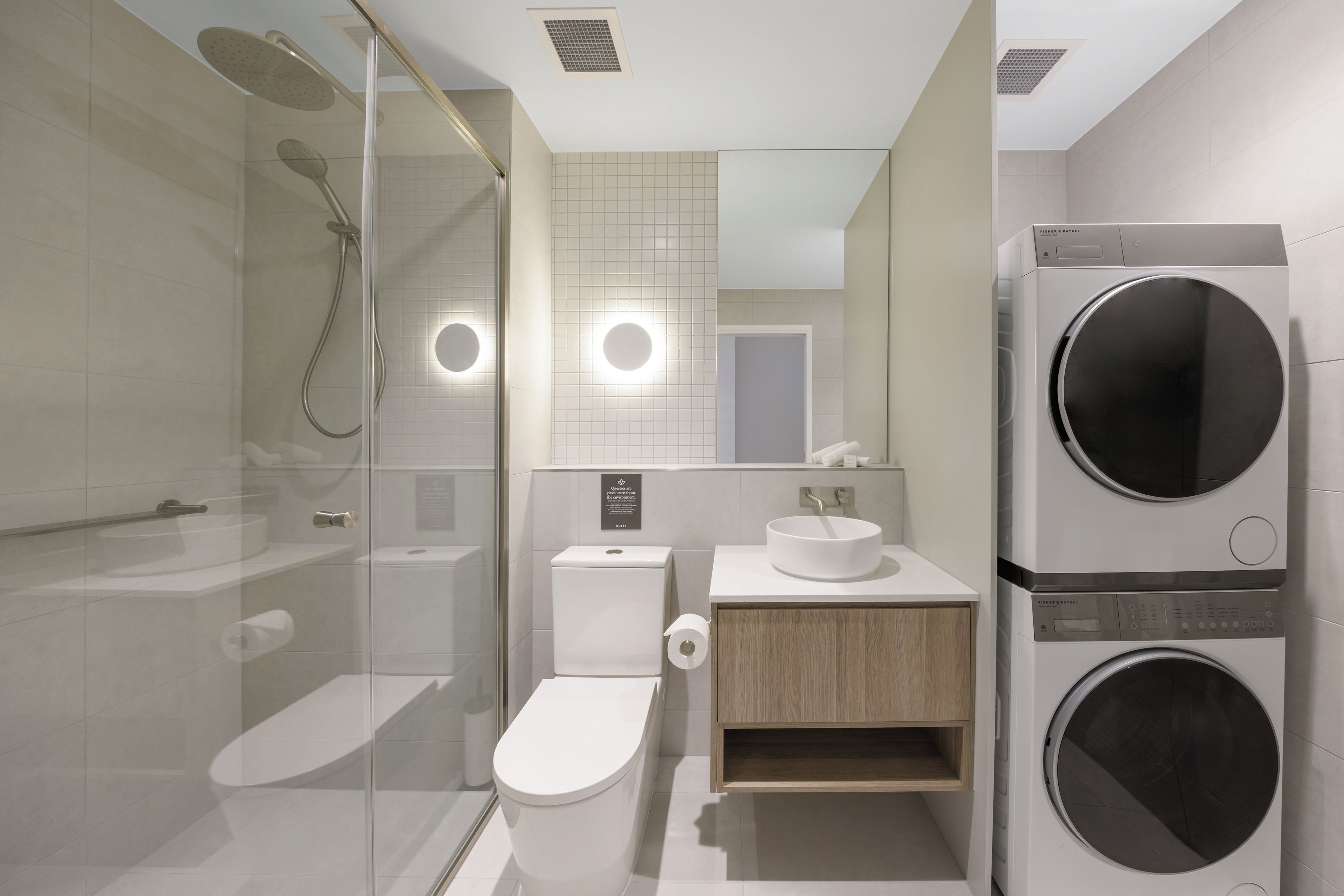 Ein modernes Badezimmer mit Duschkabine, Toilette, Waschbecken mit Spiegel sowie integrierter Wasch- und Trockenmaschine.