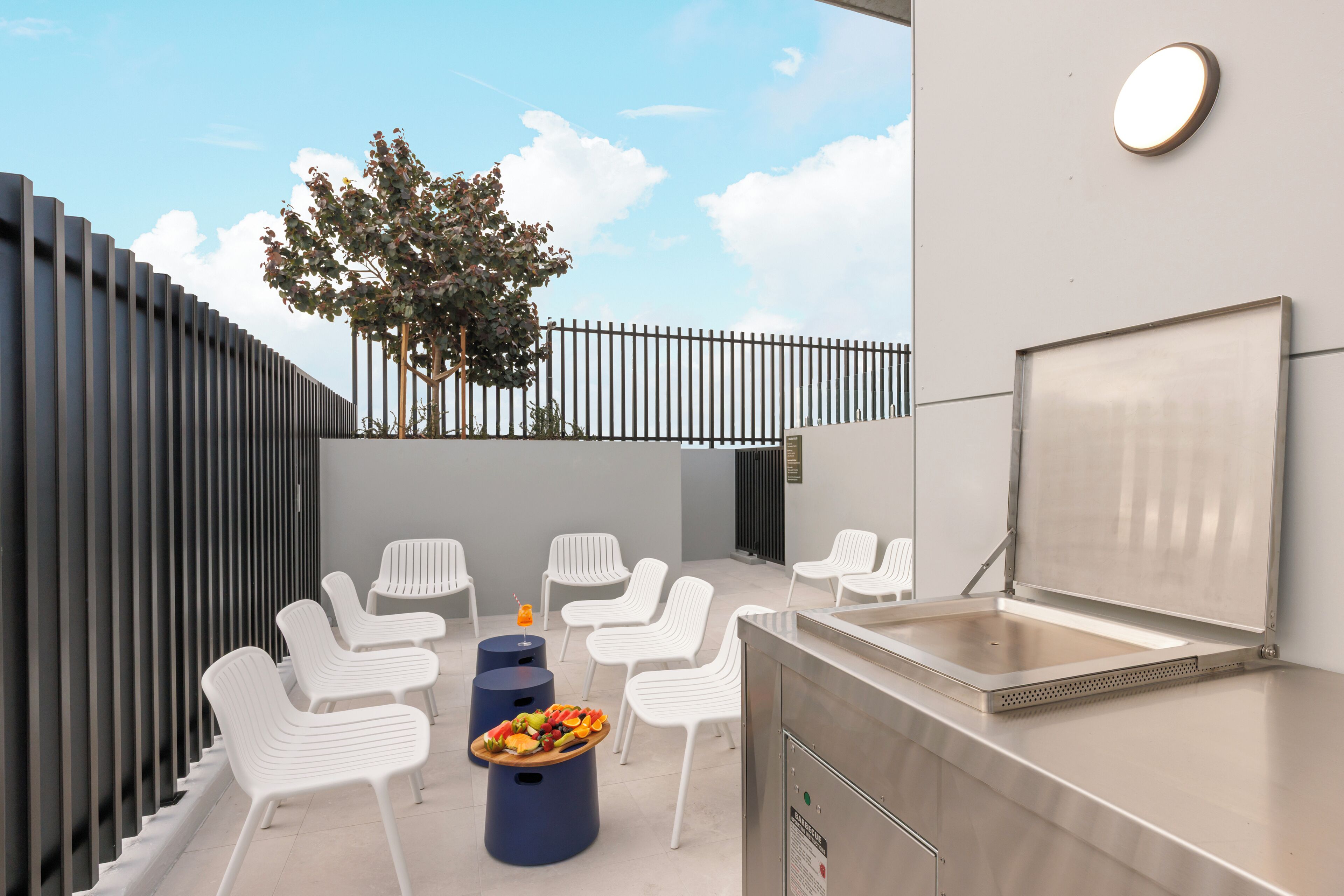 Un espacio al aire libre con sillas blancas, una parrilla y una bandeja de frutas.