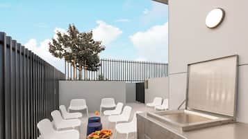 An outdoor seating area with white chairs, a barbecue grill, and a fruit platter.