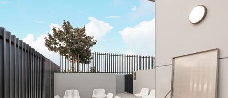 An outdoor seating area with white chairs, a barbecue grill, and a fruit platter.
