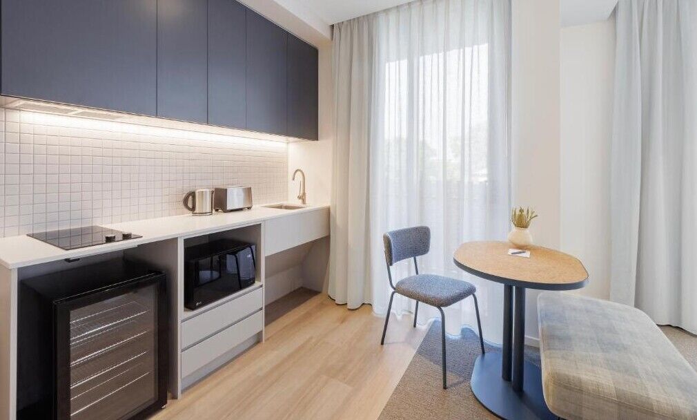 A modern kitchen with a microwave, coffee maker, and a small refrigerator. There is a dining area with a round table and two chairs.