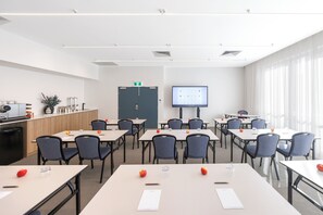 A conference room with tables, chairs, a projector screen, and a kitchenette area. - Quest Southport (Southport)