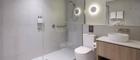 Un baño moderno con ducha de vidrio, inodoro y tocador con lavamanos.