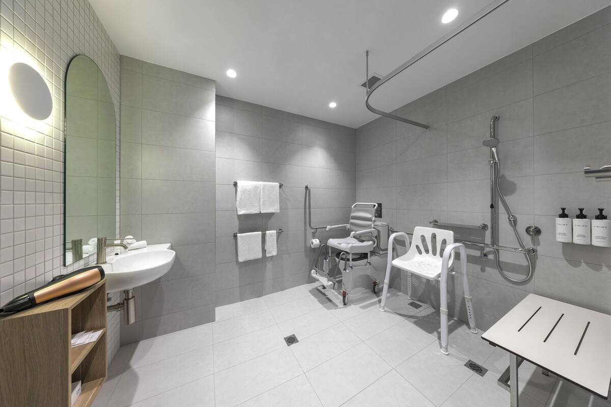 Un bagno moderno con lavandino, specchio, doccia e una sedia per disabili.