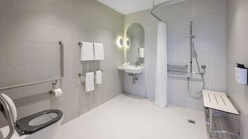 Une salle de bain moderne équipée de toilettes, de barres d’appui, d’un lavabo, d’une douche et d’un miroir.