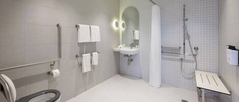 A modern bathroom with a toilet, grab bars, a sink, a shower, and a mirror.